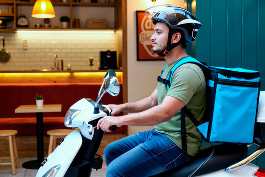 Young adult Caucasian man riding scooter with insulated delivery backpack, working food courier shift for last mile service. Ideal for gig economy, app delivery, urban logistics marketing