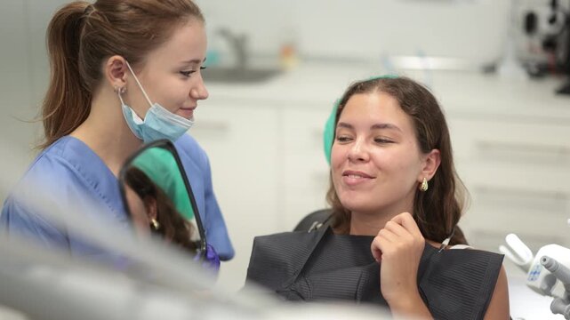 Joyful young woman in dentist office looking at her healthy teeth in the mirror. Woman dentist shows a client clean teeth. High quality 4k footage