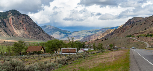 A wide panoramic landscape of a mountain range under a dramatic, overcast cloudy sky with green fields in the foreground. © Pisit