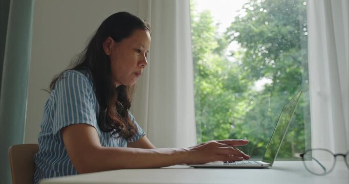 Asian middle woman wear glasses typing work on computer, using working with laptop at home office