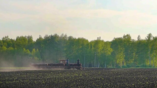Sowing equipment working on agricultural field near forest during spring planting season and seasonal farming operations