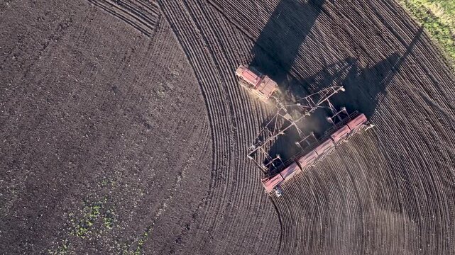 Old tractor and seed drill creating curved field patterns during spring planting, aerial farmland texture with large copy space and long evening shadows