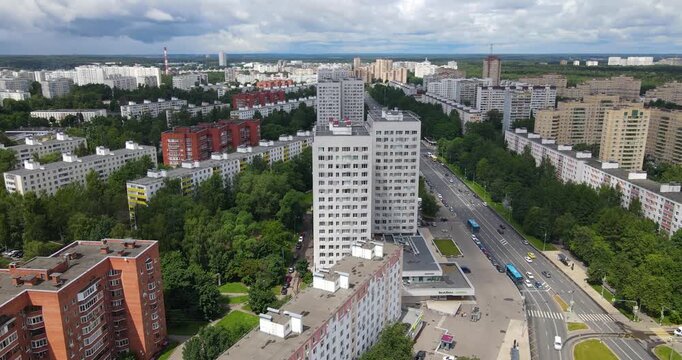 Aerial orbiting shot around a modern white residential tower surrounded by brick apartment blocks and a green park area