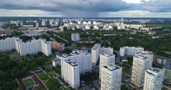 Aerial pull-back shot of a green residential district in Zelenograd under dark dramatic clouds with visible rain approaching in the distance