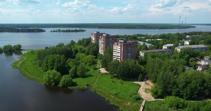 Cinematic aerial orbiting shot of tall red brick apartment buildings situated on a green peninsula next to a wide river in Konakovo 