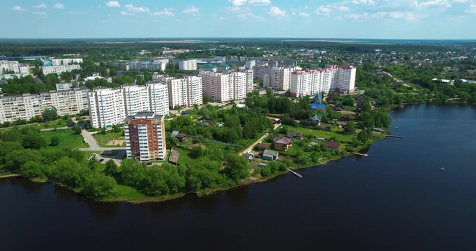 Aerial orbiting shot of a green provincial town featuring a football pitch, residential neighborhoods, and a large power plant in the distance