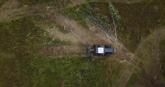 Top-down aerial shot directly over a heavy forestry mulcher tractor cutting a path through tall grass and small trees