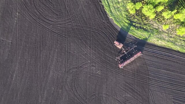 Drone top view of sowing machine working across agricultural field with soil patterns and cultivated farmland texture