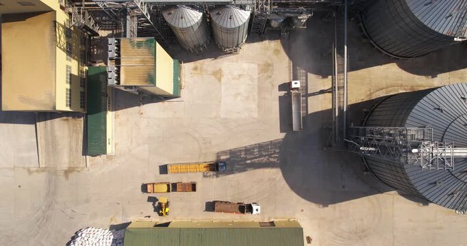 Aerial descending top-down shot of a large industrial grain elevator facility with massive metal storage silos and trucks