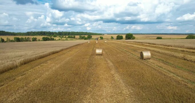 Low altitude aerial shot focusing on a round straw hay bale sitting in a golden harvested field after seasonal harvesting operations