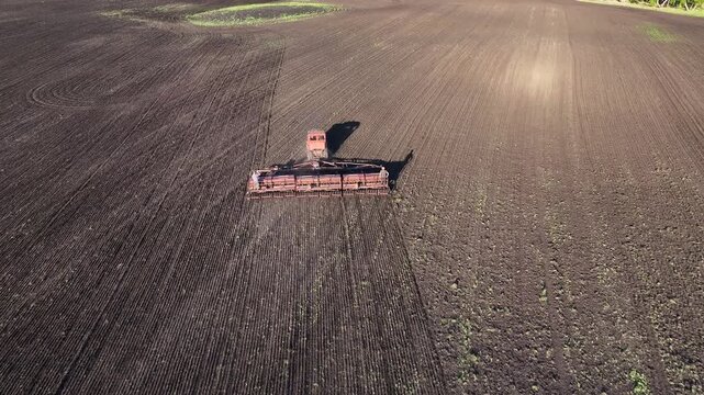 Farm workers monitoring seed drill during sowing operations on large agricultural field aerial drone view of spring farming and cultivated farmland