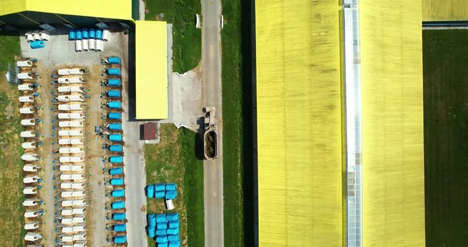 Top-down aerial view of a modern dairy farm showing rows of plastic calf hutches next to a bright yellow barn roof