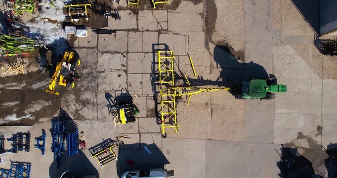 Aerial descending top-down view of various agricultural tractors and farming implements parked on a concrete farmyard