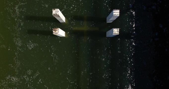 Top-down aerial view directly over square concrete foundation piles with exposed rebar installed in dark green water