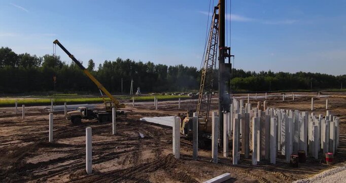 Cinematic aerial orbiting shot around a heavy pile driving rig installing concrete foundation pillars on a muddy construction site