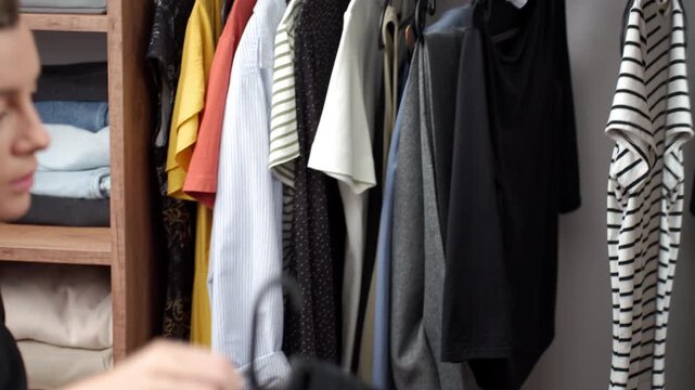 Woman choosing clothes for work in front of a wardrobe mirror taking a garment from a hanger. Concept of outfit choice personal style and everyday fashion.