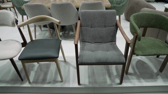 Video shows a slow pan across a modern furniture showroom featuring diverse dining chairs in gray, green, black, white. Wooden frames upholstered seats are highlighted under bright lighting