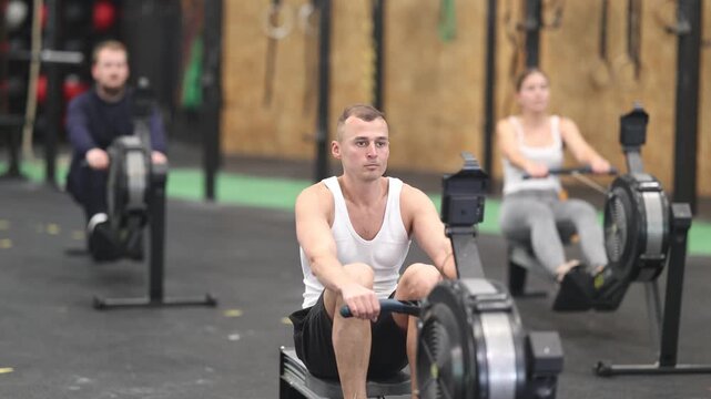 Concentrated young adult man doing high intensity full body workout in gym, exercising on rowing machine . High quality 4k footage