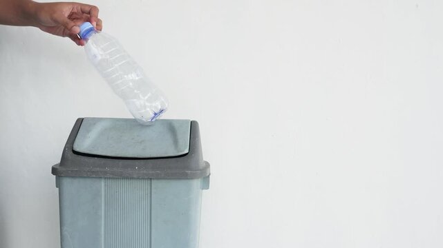 Close-up of a hand throwing a used bottle into a trash can. The concept of disposing of trash properly.