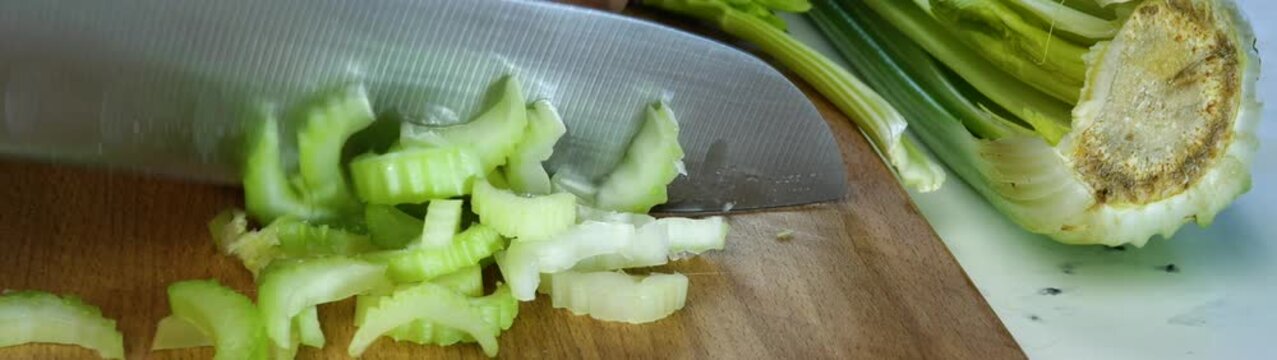 Cutting fresh celery on a wooden cutting board making healthy food choices for meal preparation.