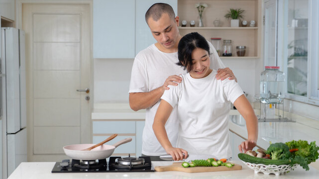 Loving Husband Embracing Wife While Chopping Fresh Vegetables in Kitchen