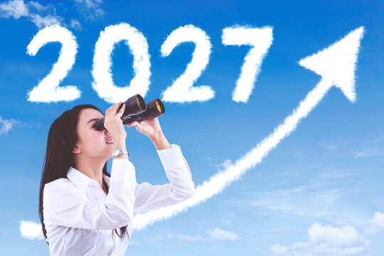 Businesswoman Looking Through Binoculars at Year 2027 and Rising Growth Arrow in the Sky