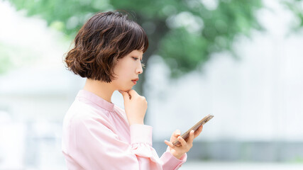 スマートフォンを使いながら考えるビジネスウーマン, Businesswoman Thinking While Using a Smartphone © Trickster*