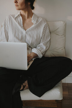 Woman seated with laptop on sofa, striped shirt, warm minimalist interior, soft light and calm vibe