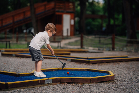 Little boy playing mini golf outdoors focused on game