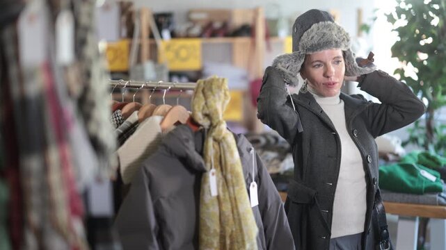 Adult woman buyer choosing warm winter fur hat in clothing store
