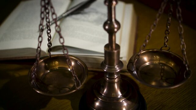 A brass scale of justice figurine with a sword placed on a wooden surface with law books and warm atmospheric lighting in the background.