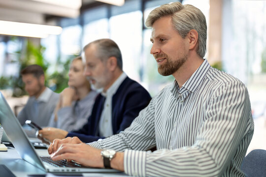Four business professionals using laptop on desk discussing strategy company