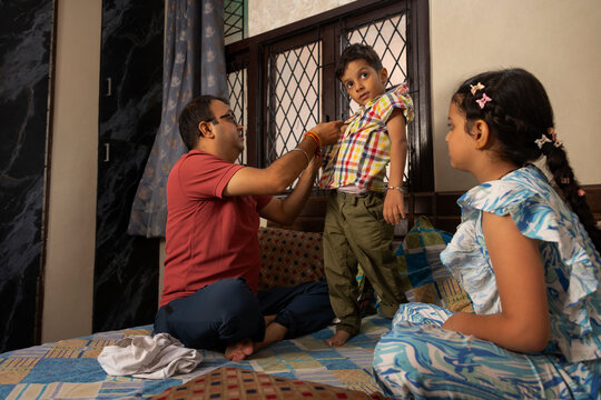  daughter seeing her father helping his son buttoning up his shirt in bedroom