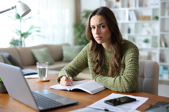 Worried teleworker writing in agenda looking at you working at home