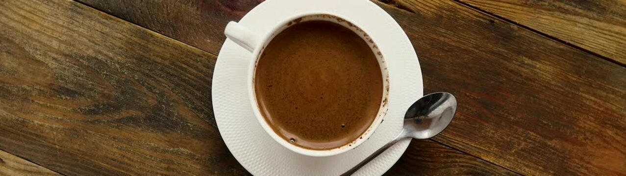 Coffee cup and saucer with a spoon rotating on a rustic wooden table offering a warm morning beverage experience.
