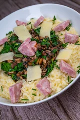A bowl contains a serving of mushroom and spinach risotto. On top are pieces of Morteau sausage and parmesan cheese. The dish is placed on a wooden surface. © FreeProd