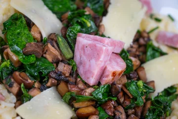 A bowl contains a serving of mushroom and spinach risotto. On top are pieces of Morteau sausage and parmesan cheese. The dish is placed on a wooden surface. © FreeProd