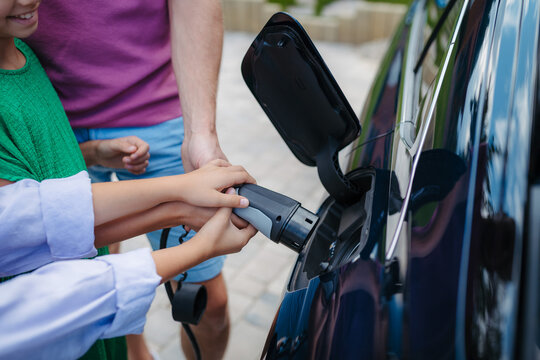 Close up of kids hands helping mom to charging electric car.