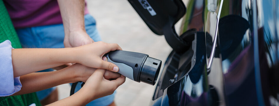 Close up of kids hands helping mom to charging electric car.