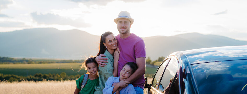 Happy family on car trip having break in nature, next their electric car.