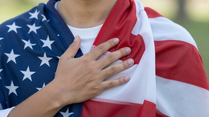 Close-up of a person placing their right hand over their chest while draped in an American flag, symbolizing patriotism and respect.