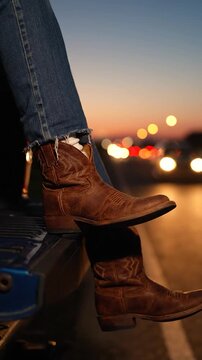 Brown leather cowboy boots rest on a truck tailgate at sunset