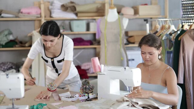 Qualified dressmakers work in a sewing workshop. Fashion designer stands near the table and draws patterns on paper next to the seamstress. High quality 4k footage