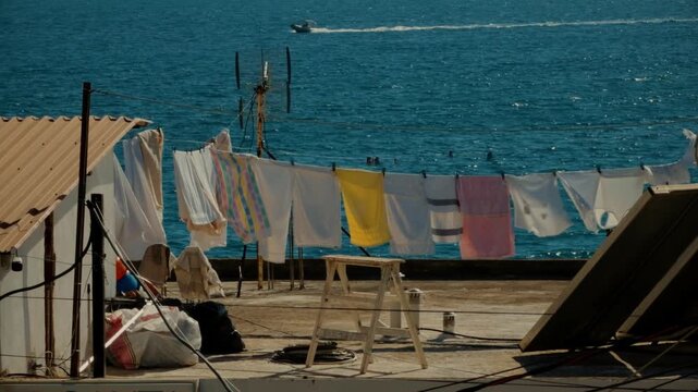 Colorful Laundry Wet Clothes Hanging On Clothesline On House Roof Terrace Against Blue Sea Water. Household Chores