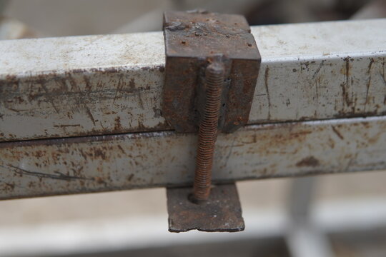 Close-up of a rusty metal screw bolt clamp locking two iron square bars together.