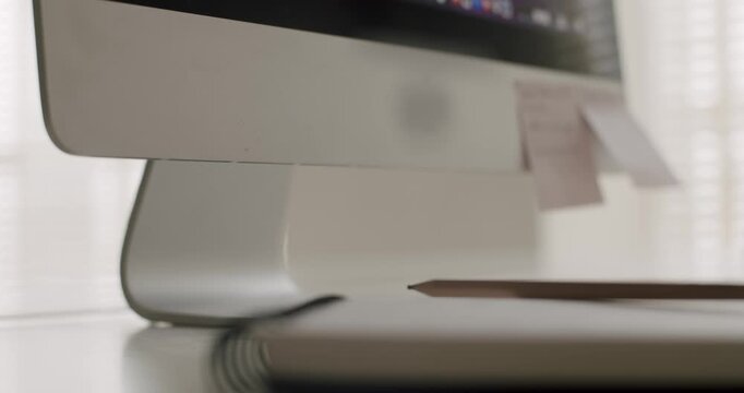 Woman hand sticking a handwritten pink adhesive note on a modern desktop computer monitor at her workplace desk, a useful reminder for managing tasks and deadlines for a business project