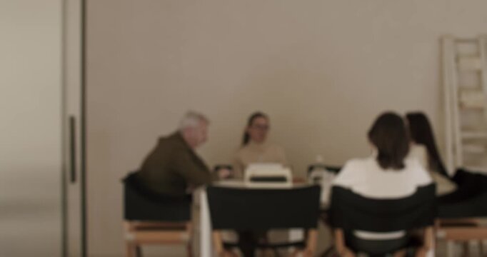 Blurry slow motion shot of a creative team of coworkers brainstorming ideas during a corporate business meeting, discussing a new project while sitting together around a table