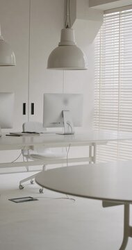 Bright, clean, and minimalist office space with modern white furniture, computers, and large pendant lamps, creating a professional and contemporary workspace ideal for corporate concepts. vertical