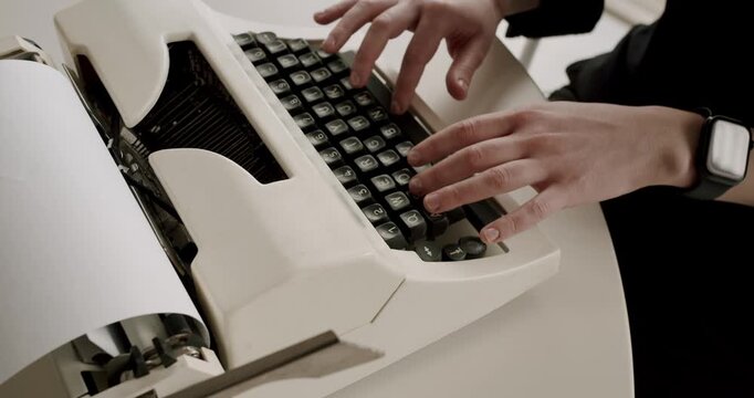 Top-down slow-motion view of a writer's hands typing on the keys of a retro typewriter, creating a document, novel, or letter with classic, old-fashioned mechanical technology at a desk