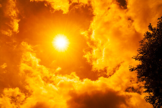 Dramatic blazing sun shining through fiery orange clouds during an extreme heatwave, global boiling and climate crisis concept, hot summer weather background.